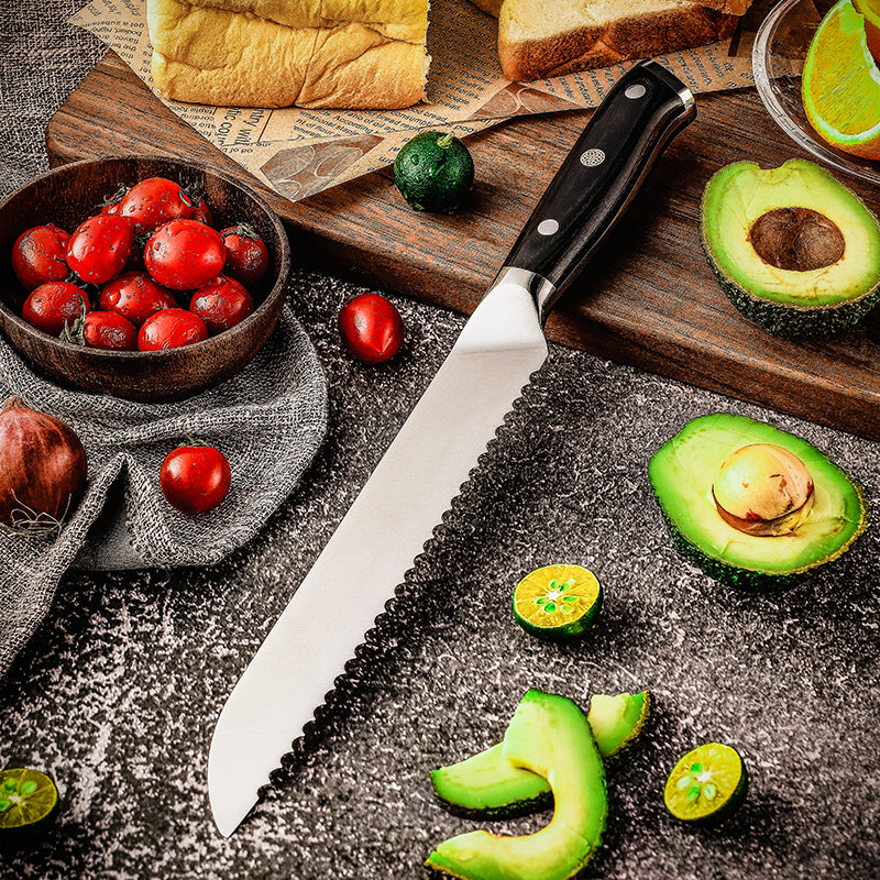 Professional Kitchen knife for bread german steel and black handle on a dark surface with sliced avocados, tomatoes, and bread.