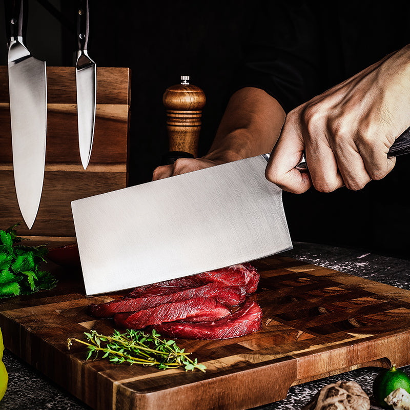 Chef cutting raw meat on a wooden cutting board with german steel cleaver branded Hikari Knife and seasonings in the background.