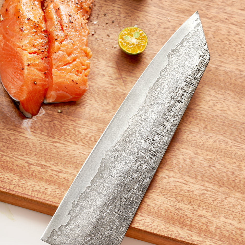 Chef's knife with Damascus pattern on a wooden cutting board with salmon and lime.