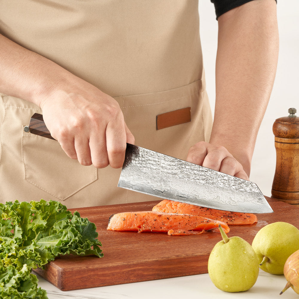 Person cutting vegetables on a wooden board with a chef's knife, wearing a beige apron.