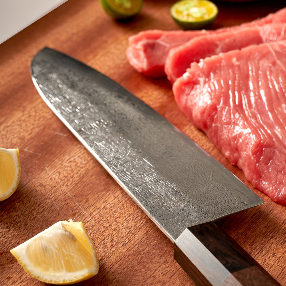 Chef's knife on a wooden cutting board with raw meat and lemon slices