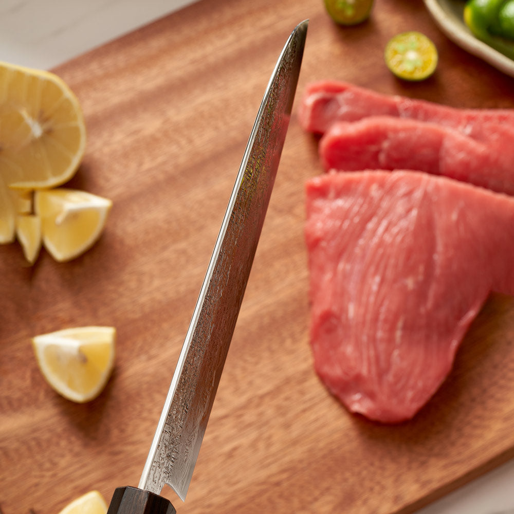 Santoku Knife on a wooden cutting board with lemons and limes