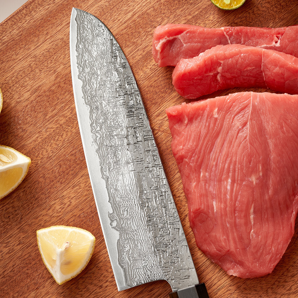 Chef's knife on a wooden cutting board with raw meat and lemon wedges