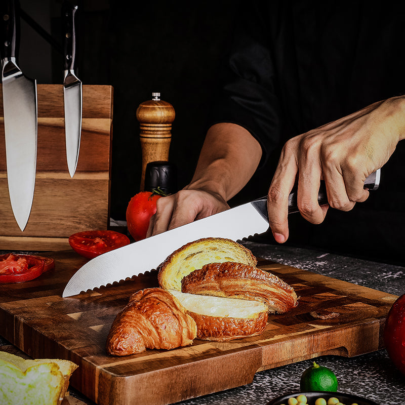 Person slicing bread on a wooden cutting board with german steel bread knife branded Hikari and ingredients in the background.