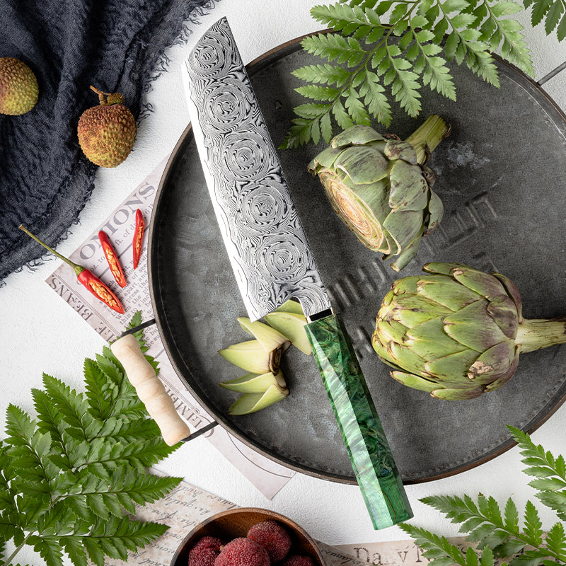 Decorative Rose Damascus Pattern knife with green handle on a plate with artichokes, surrounded by ferns and other items.