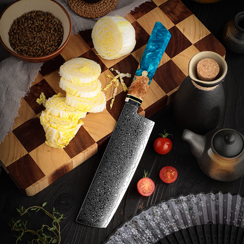 Wooden cutting board with sliced cabbage, a large nakiri knife, japanese knife, professional knife and various kitchen items on a dark surface.