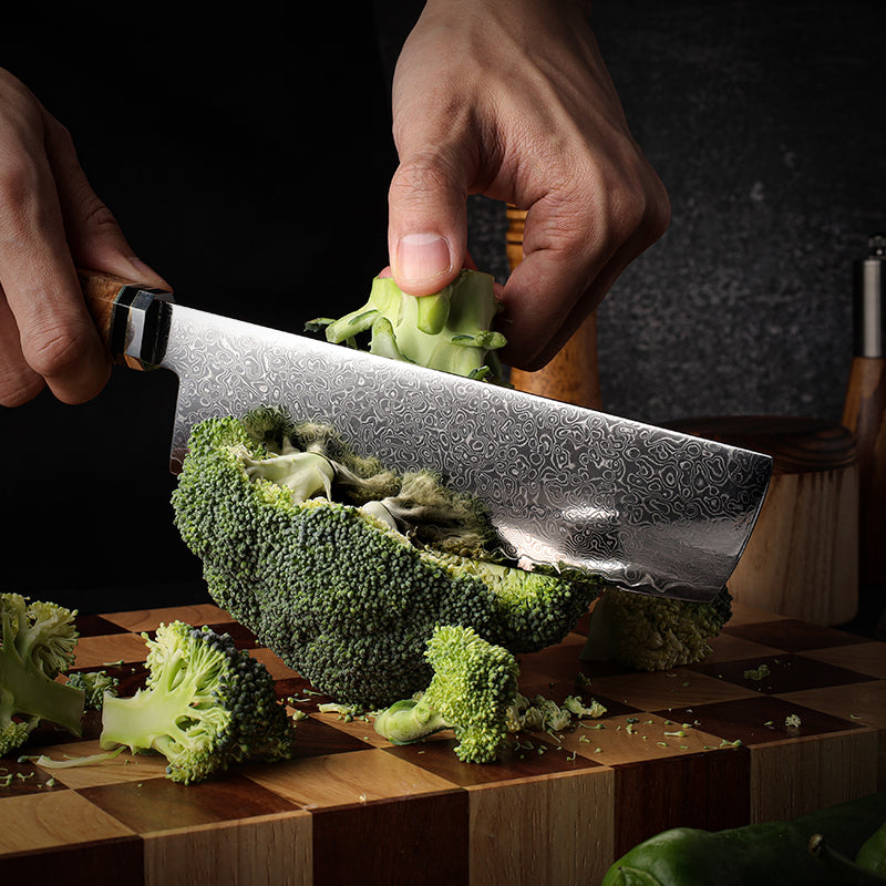 Person cutting broccoli with a japanese knife on a wooden cutting board.